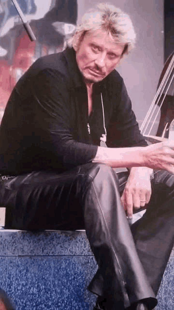 a man in a black shirt and leather pants is smoking a cigarette while sitting down .