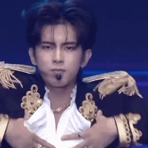 a young man in a black and gold jacket is holding his chest and making a funny face .