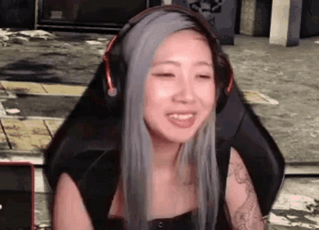 a woman with gray hair is wearing headphones and smiling while sitting in a gaming chair .