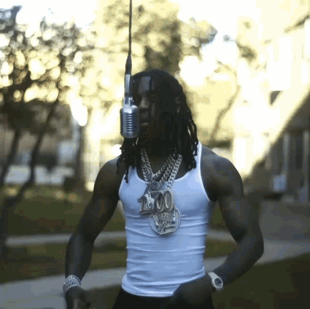 a man with dreadlocks is wearing a white tank top and holding a microphone with the number 100 on it
