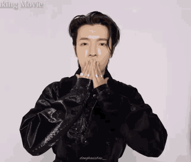 a man in a black leather jacket is making a heart with his hands .