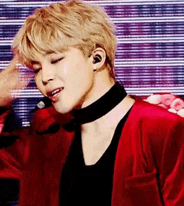 a young man wearing a red jacket and a black choker is standing on a stage .