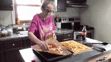 a woman in a pink shirt with the word hawaiian on it prepares a pizza and french fries