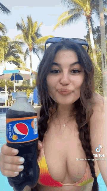 a woman in a bikini is holding a bottle of pepsi in her hand .