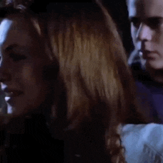 a close up of a woman 's face in a dark room with a man behind her .