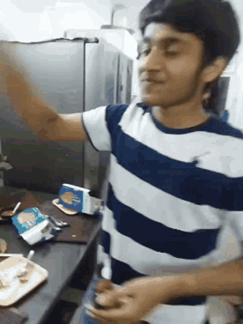 a man in a blue and white striped shirt is standing in front of a fridge