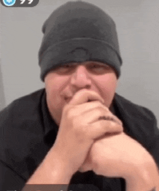 a man wearing a black hat and a black shirt is covering his mouth with his hands .