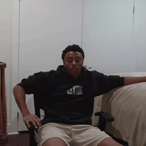 a man wearing a black hoodie that says centro sits in a chair