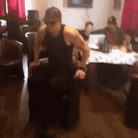 a man in a black tank top is sitting on a chair in a room with other people .