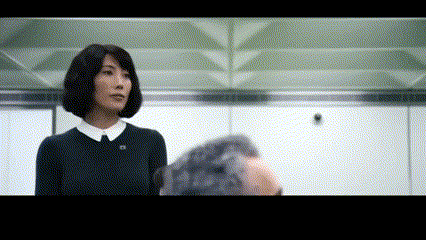 a woman in a black sweater and white collar is talking to a man in a room .