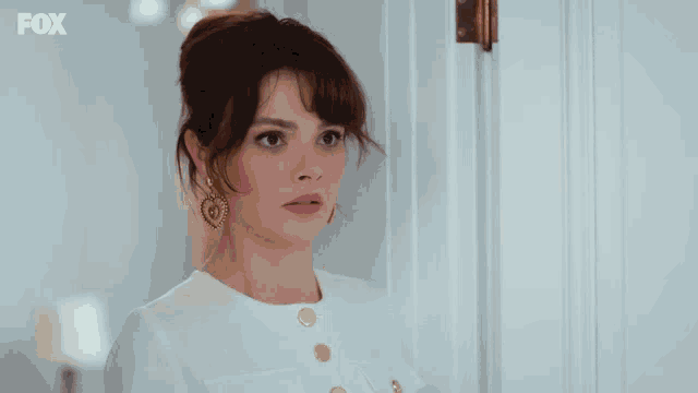 a woman in a white dress stands in front of a door with fox written on the bottom