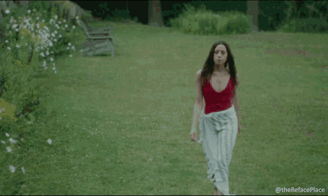 a woman in a red top and white striped skirt is walking in a field