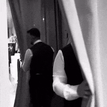 a man in a tuxedo is standing behind a curtain