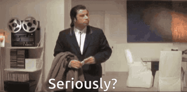 a man in a suit and tie is standing in a living room and says seriously ?