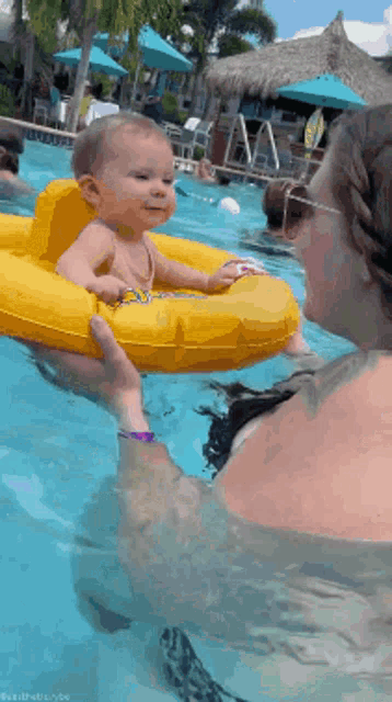 a woman holds a baby in a yellow raft in a pool