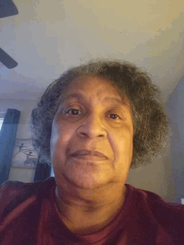 a woman with curly hair and a red shirt looks down at the camera