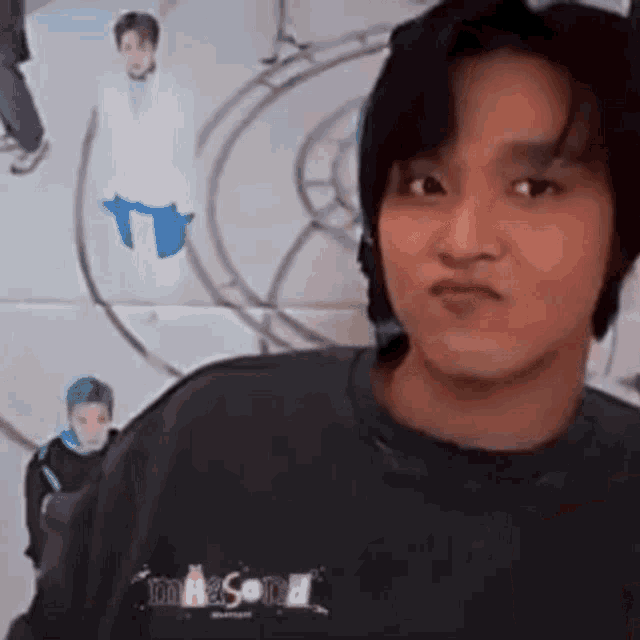 a young man wearing a black sweatshirt is making a funny face in front of a wall .