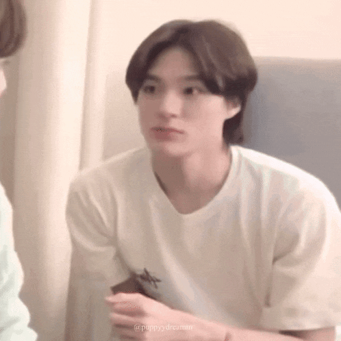 a young man in a white t-shirt is sitting on a couch and looking at the camera .