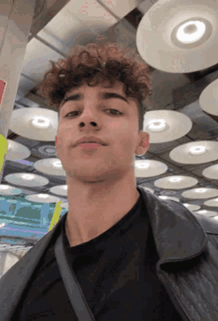 a young man with curly hair wearing a black shirt and a black leather jacket