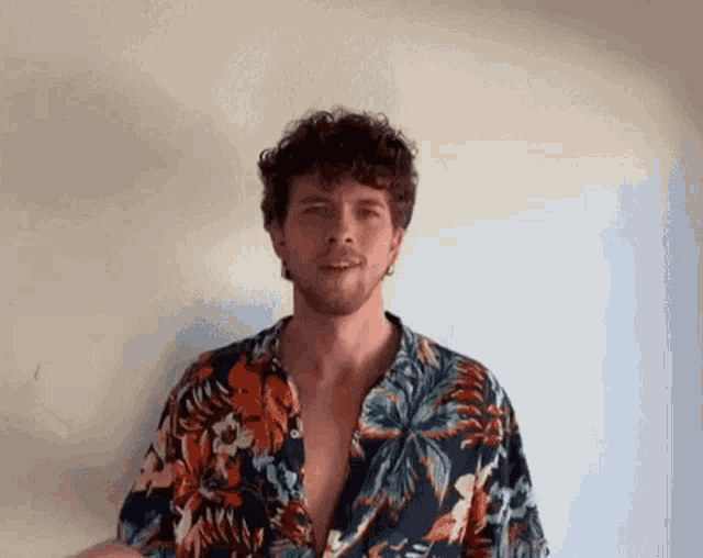 a man with curly hair and a beard wearing a colorful shirt is standing in front of a wall .