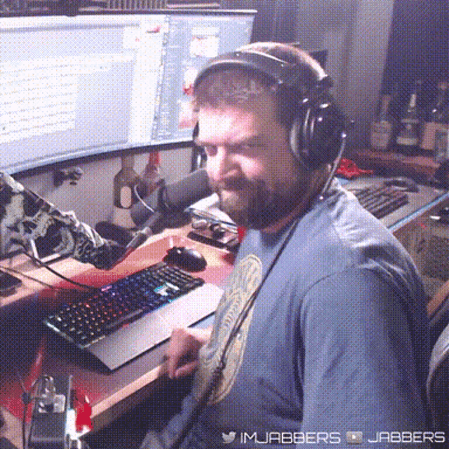 a man wearing headphones sits at a desk in front of a computer monitor and keyboard