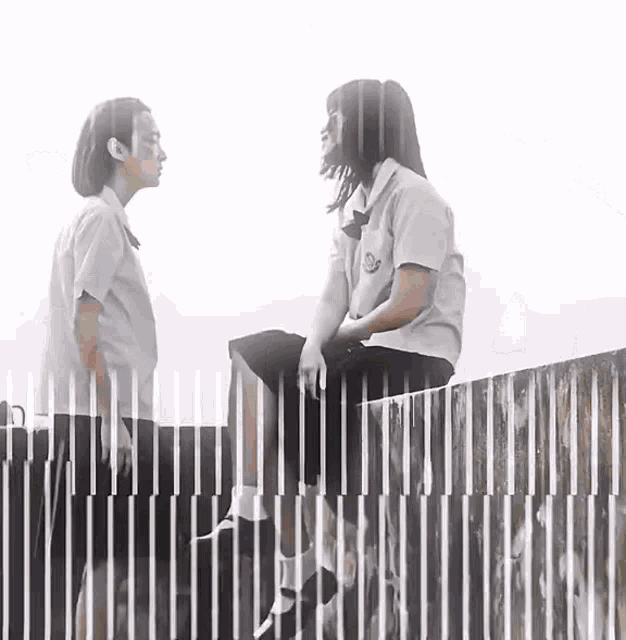 two girls in school uniforms are sitting next to each other on a fence .