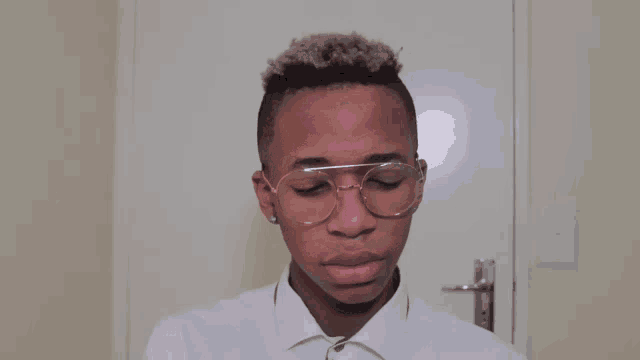 a young man wearing glasses and a white shirt is looking at the camera