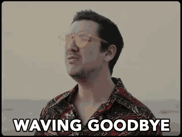 a man wearing sunglasses and a colorful shirt is saying waving goodbye .