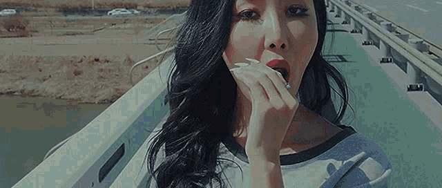 a woman is smoking a cigarette on a bridge while looking at the camera .