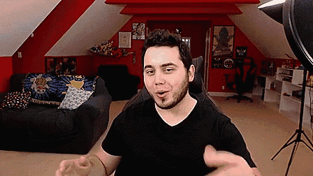 a man with a beard is sitting in front of a camera in a room with red walls