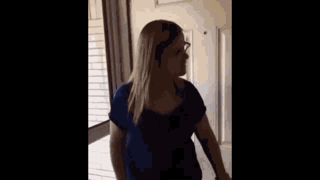 a woman in a blue shirt is standing in front of a door and talking to someone who is looking for tex .