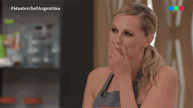 a woman covering her mouth while watching a show called master chef argentina