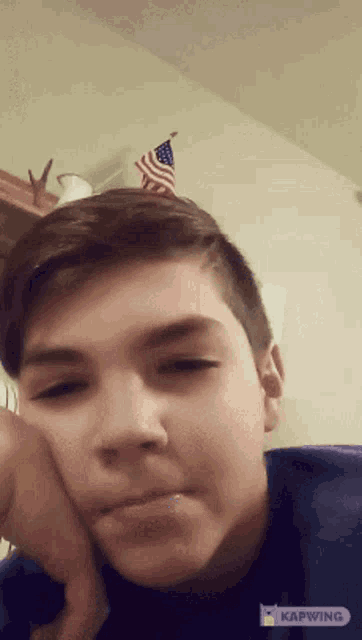 a boy is making a funny face in front of an american flag on a wall
