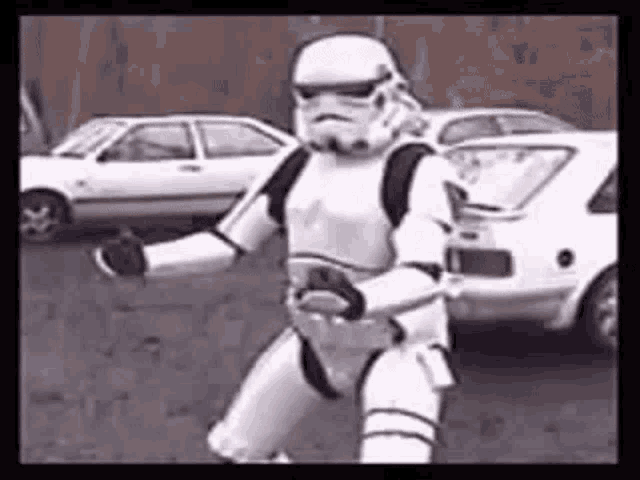 a storm trooper is dancing in a parking lot in front of a car .