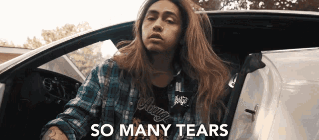 a woman in a plaid shirt is sitting in a car with the words " so many tears " above her