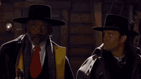 two men in hats are standing next to each other and one is holding a gun