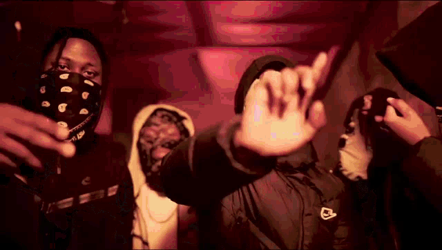 a group of men wearing masks and hoods are standing in a dark room .