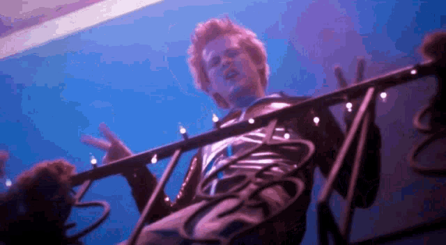 a man is sitting on a balcony with christmas lights hanging from the railing