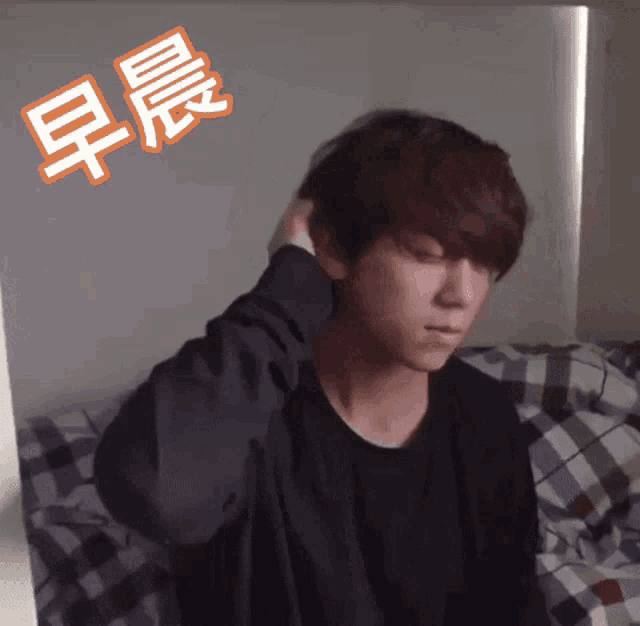 a man in a black shirt is sitting on a bed with chinese writing on the wall behind him
