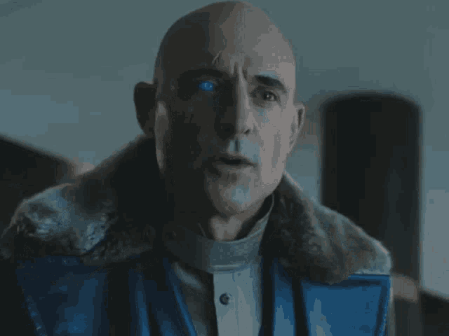 a bald man with blue eyes is wearing a blue leather jacket
