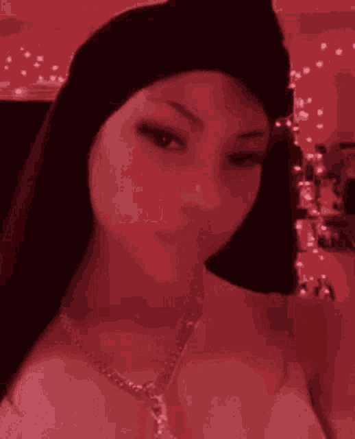 a woman is taking a selfie in a red room . she is wearing a necklace and a hat .