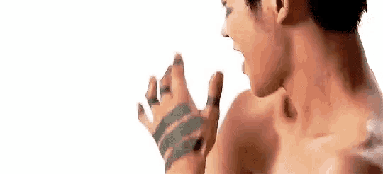 a shirtless man with a tattoo on his hand is standing with his mouth open .
