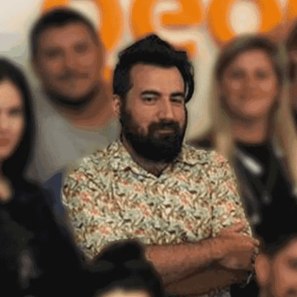 a man with a beard is sitting in a crowd with his arms crossed ..