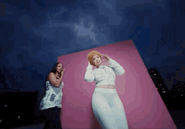 two women are dancing in front of a pink wall at night