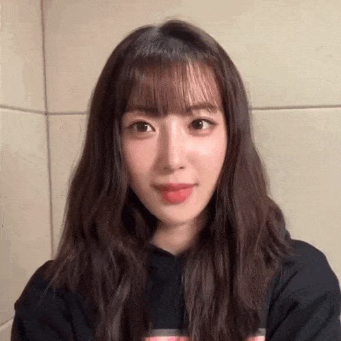 a woman with long hair and bangs is wearing a black hoodie and looking at the camera .