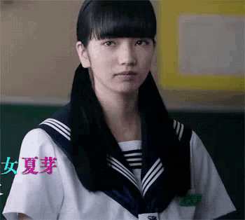 a girl in a sailor uniform is standing in front of a green board with chinese writing on it .
