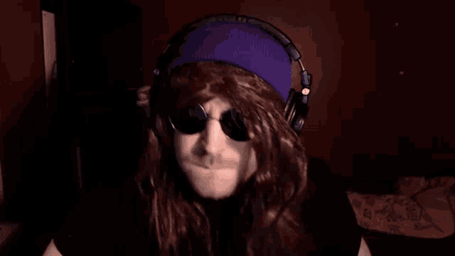 a man with long hair and sunglasses is wearing headphones and a purple headband .