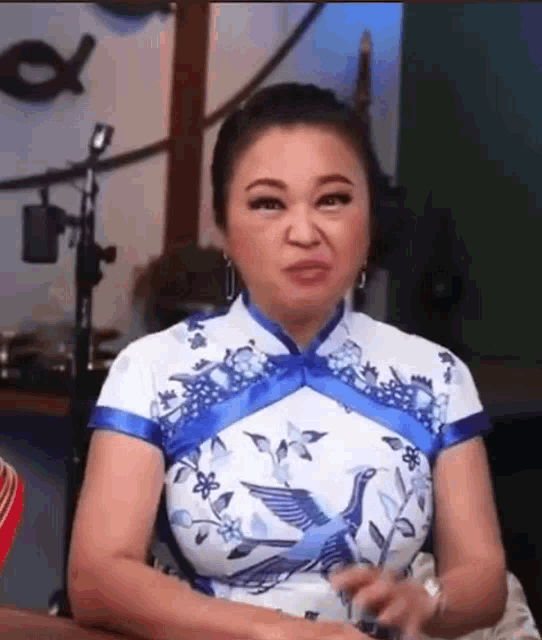 a woman in a blue and white dress is sitting at a table making a face .
