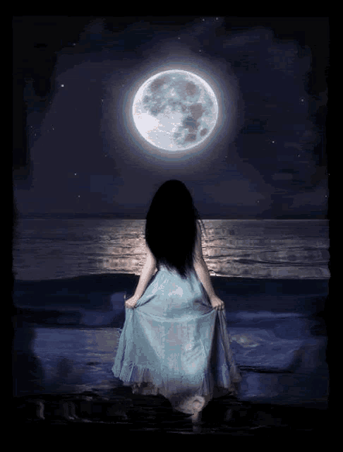 a woman in a blue dress stands on a beach looking at the moon