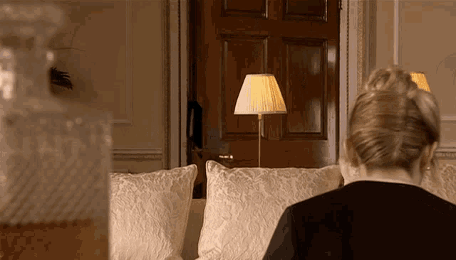 a woman sits on a couch in front of a door and a lamp